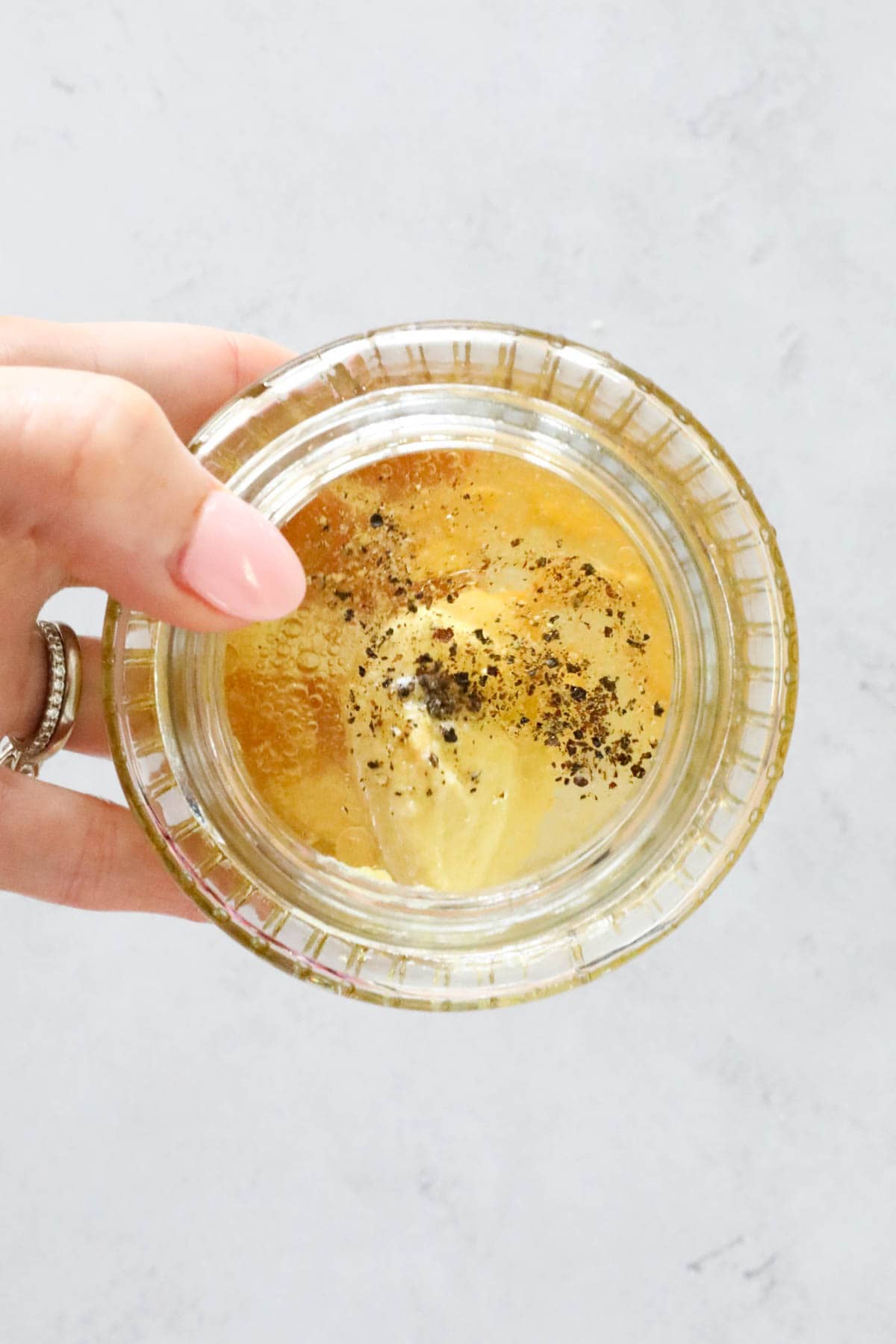 A hand holding a small jar with dressing ingredients inside.