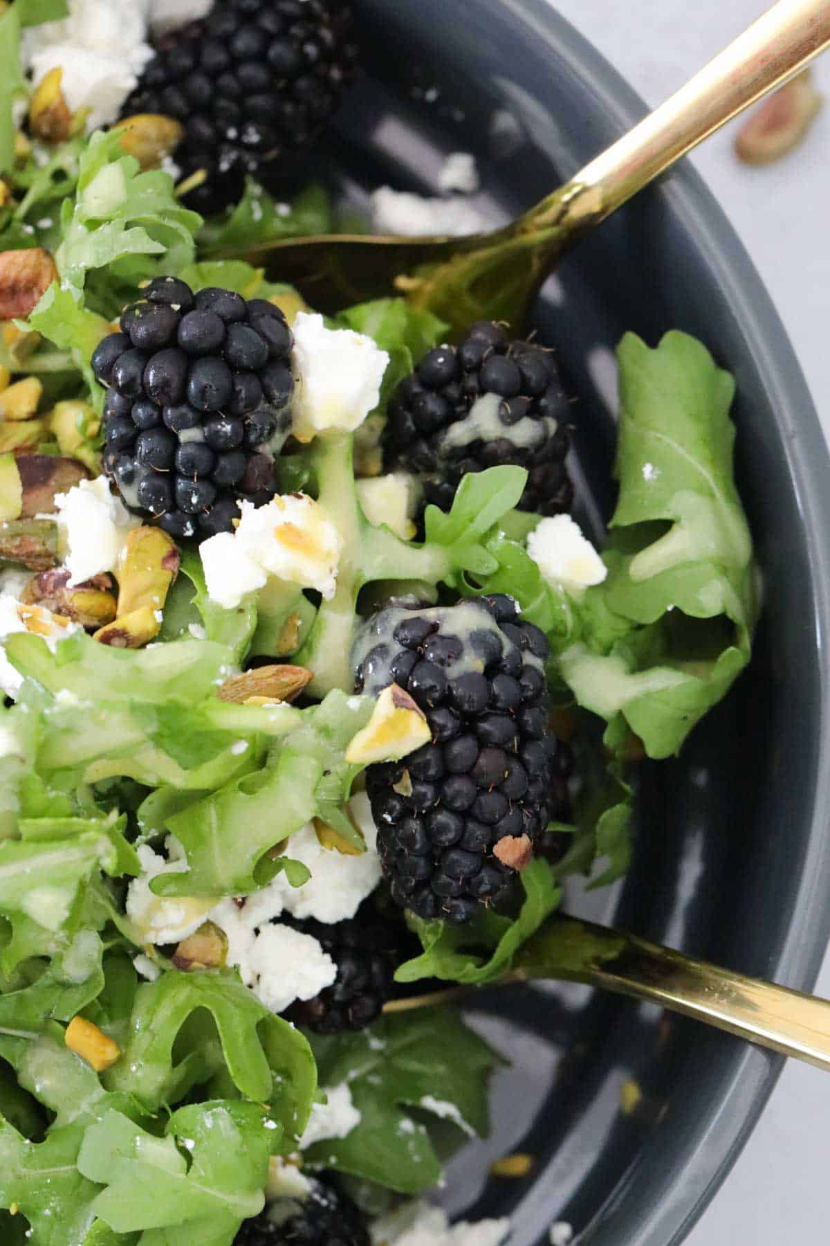 A close up of blackberry, goats cheese, pistachio and rocket salad.