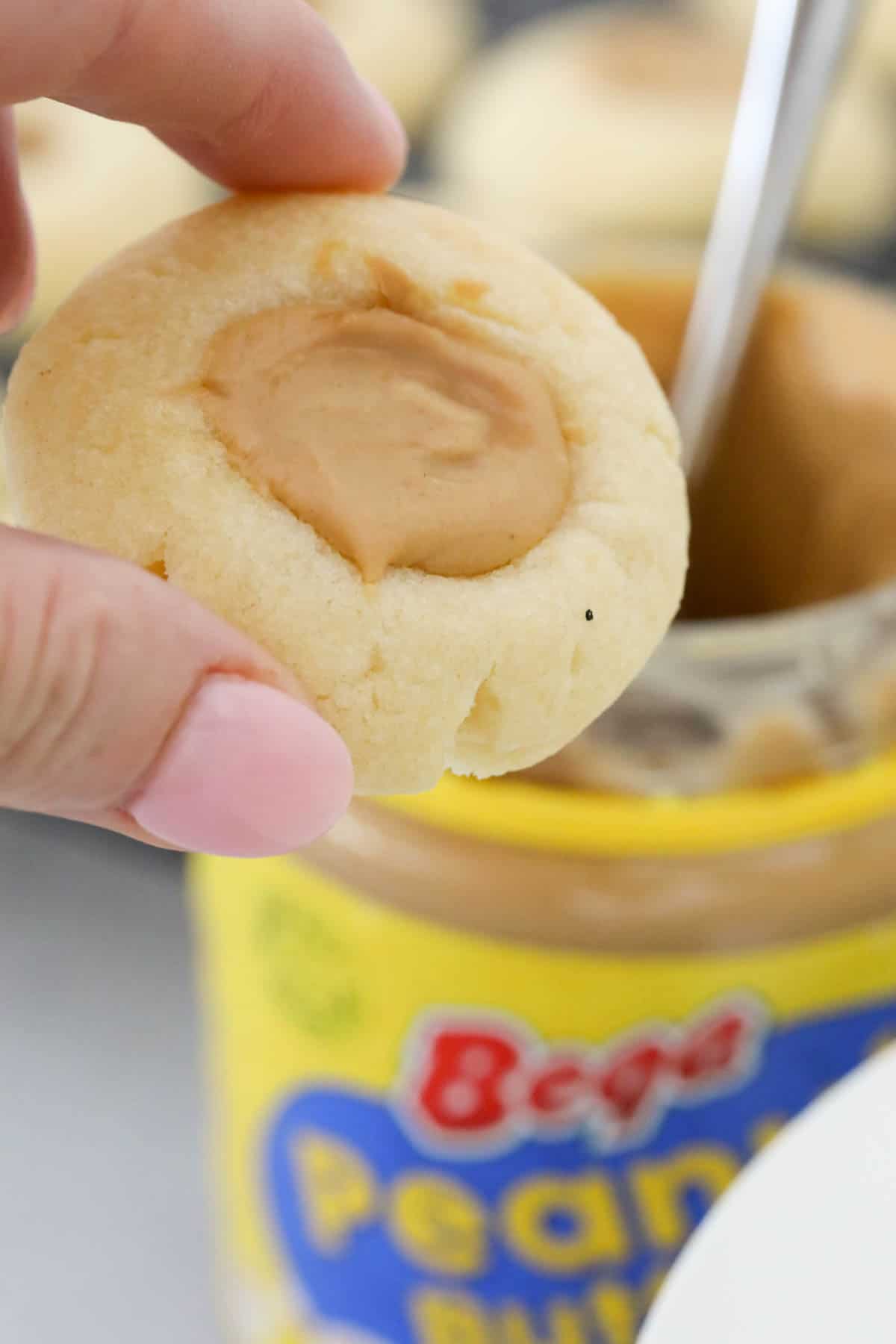 A hand holding a peanut butter thumbprint cookie above a jar.
