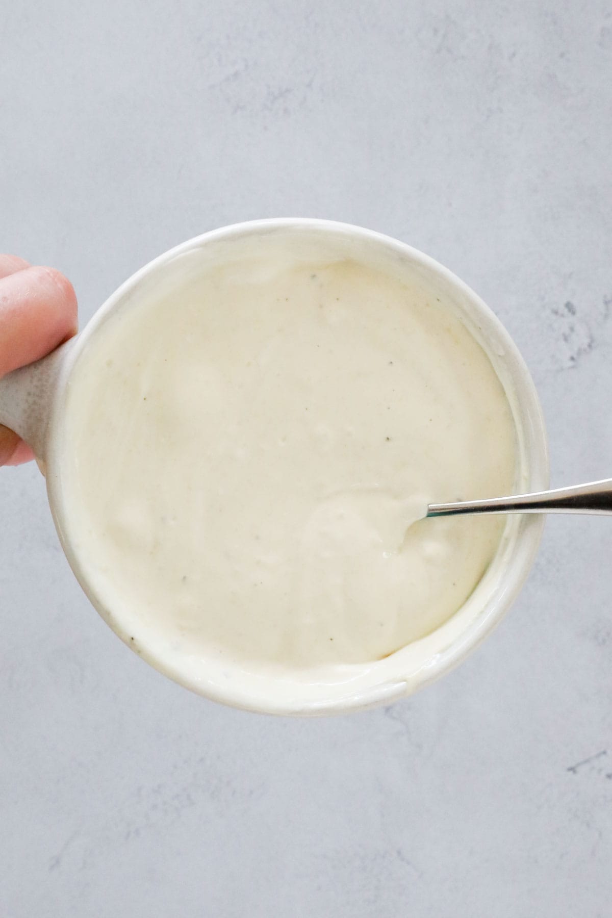 A hand holding a bowl of salad dressing.