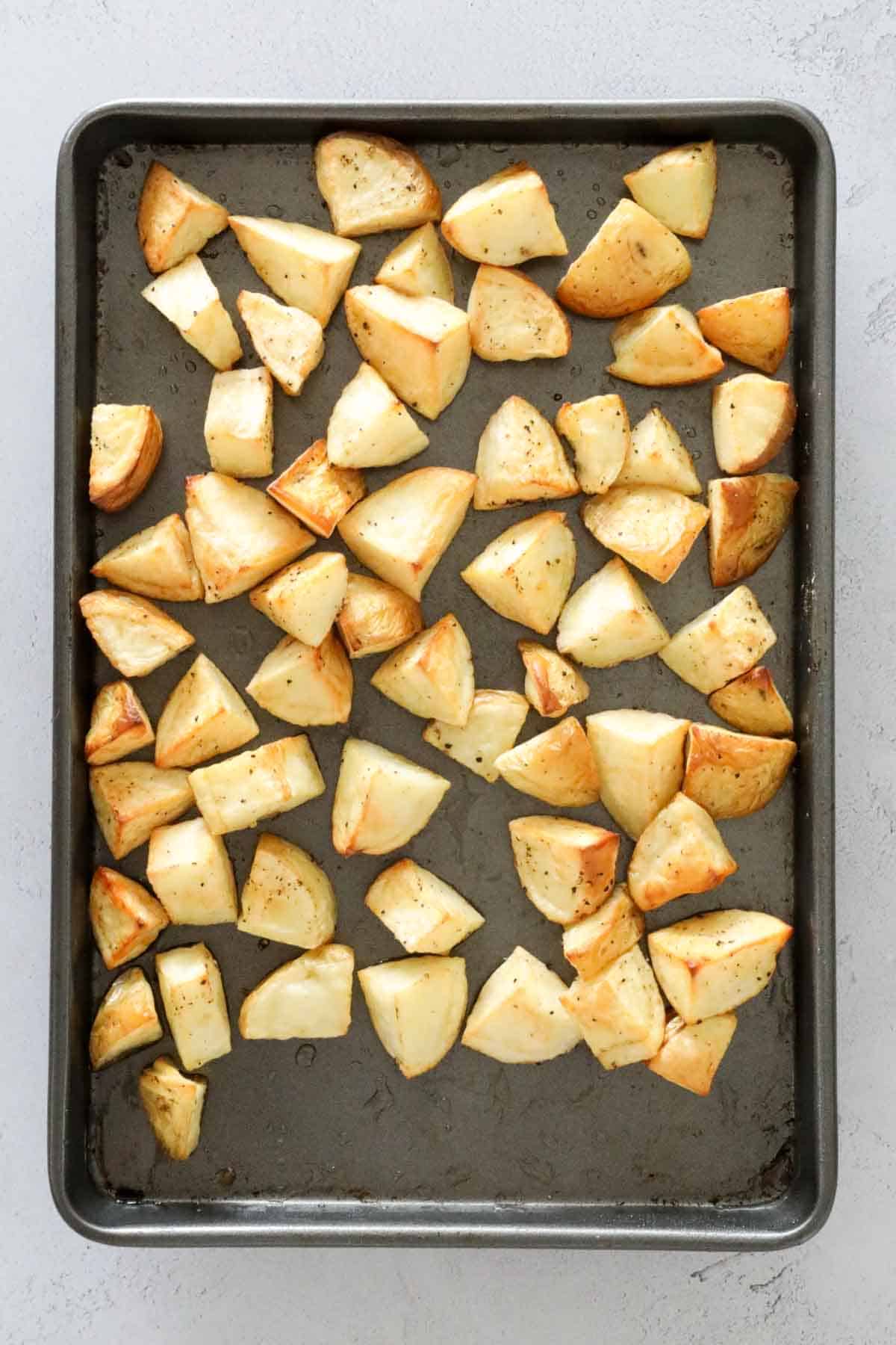 Chunks of potato roasted on a baking tray.