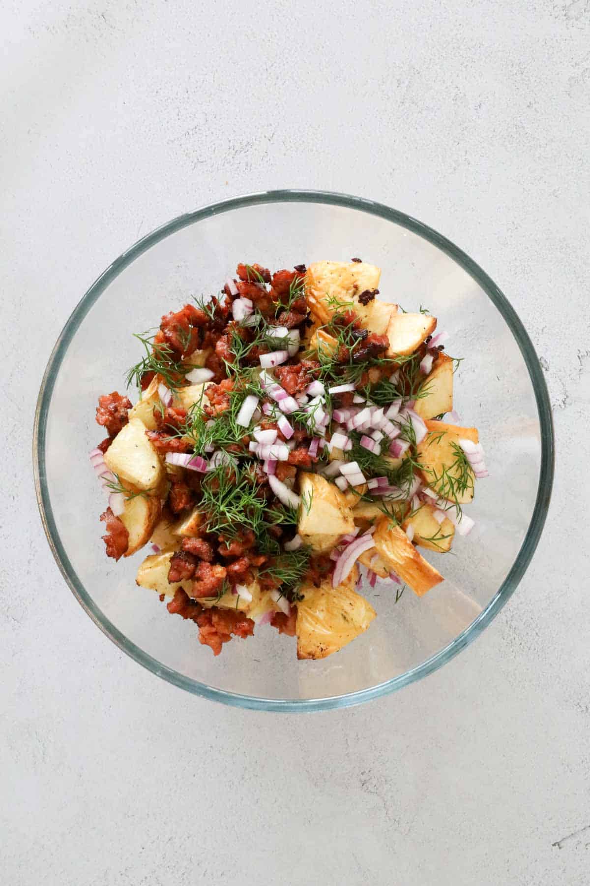 Potato chunks, fried chorizo, red onion and chopped dill in a glass bowl.