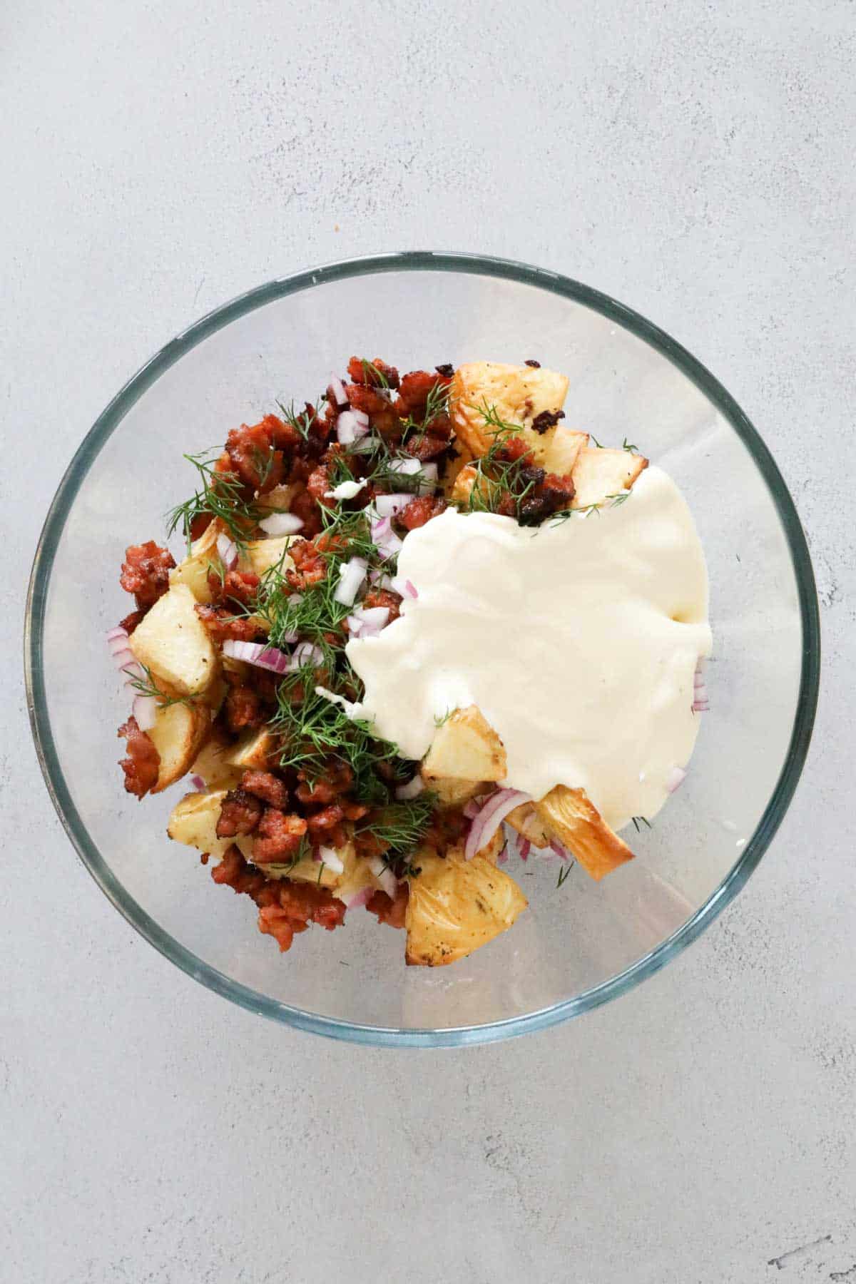 Creamy dressing added to other ingredients in a clear bowl.