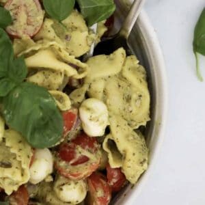 A bowl of pasta salad with tortellini, sprinkled with fresh basil leaves.