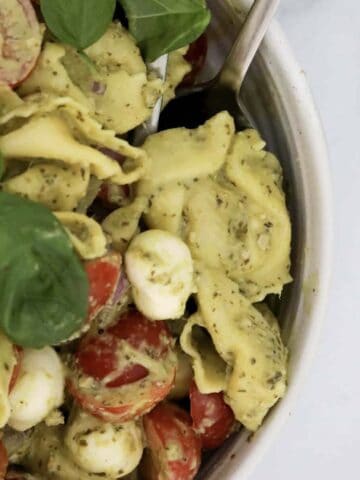 A bowl of pasta salad with tortellini, sprinkled with fresh basil leaves.