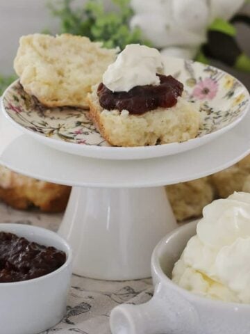 A cake stand topped with fluffy lemonade scones with whipped cream and jam.