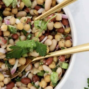 An overhead shot of bean salad with gold salad servers resting in the bowl.