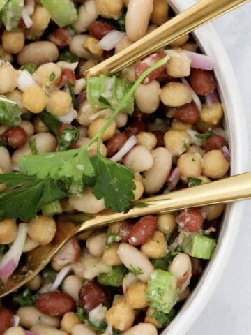 An overhead shot of bean salad with gold salad servers resting in the bowl.