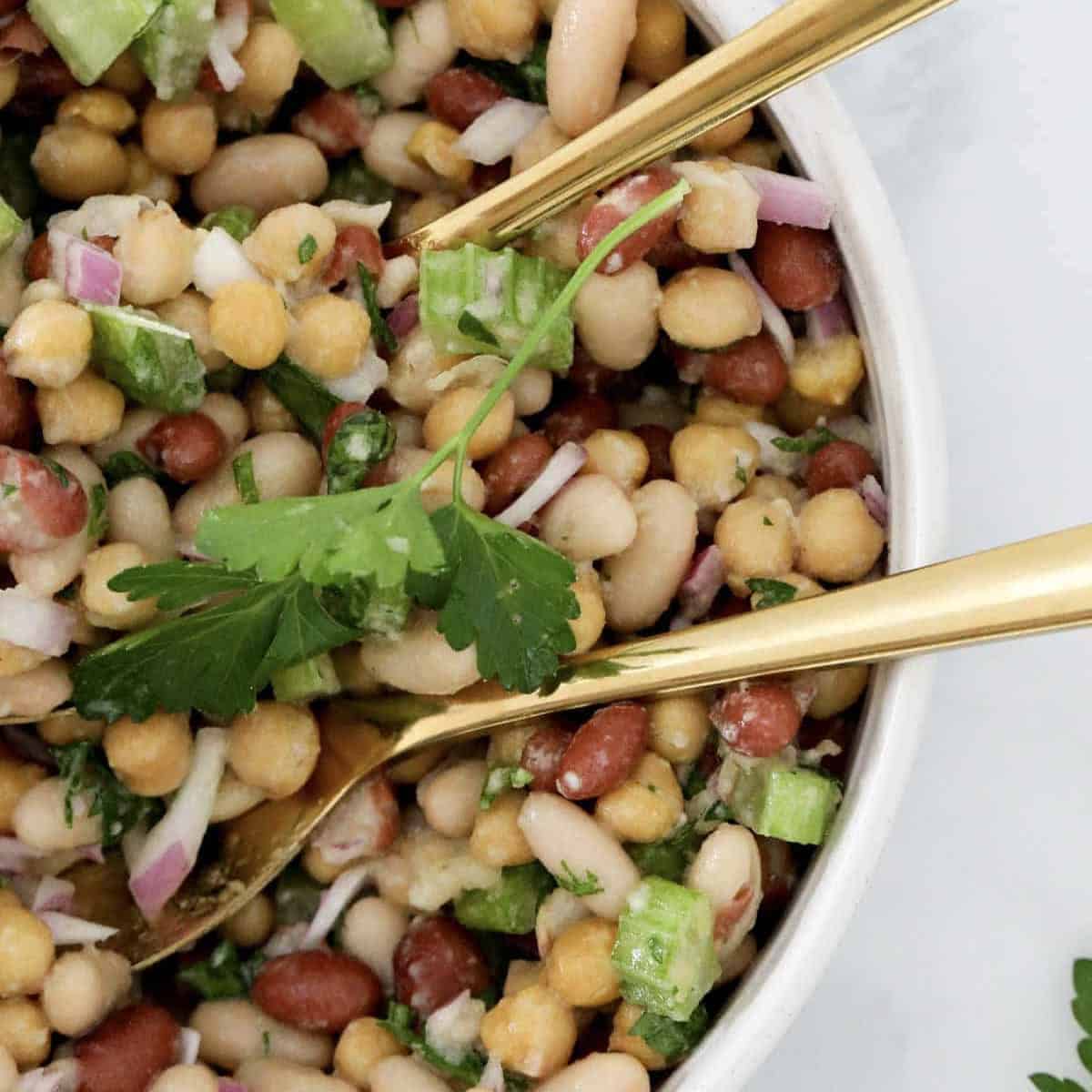 An overhead shot of bean salad with gold salad servers resting in the bowl.