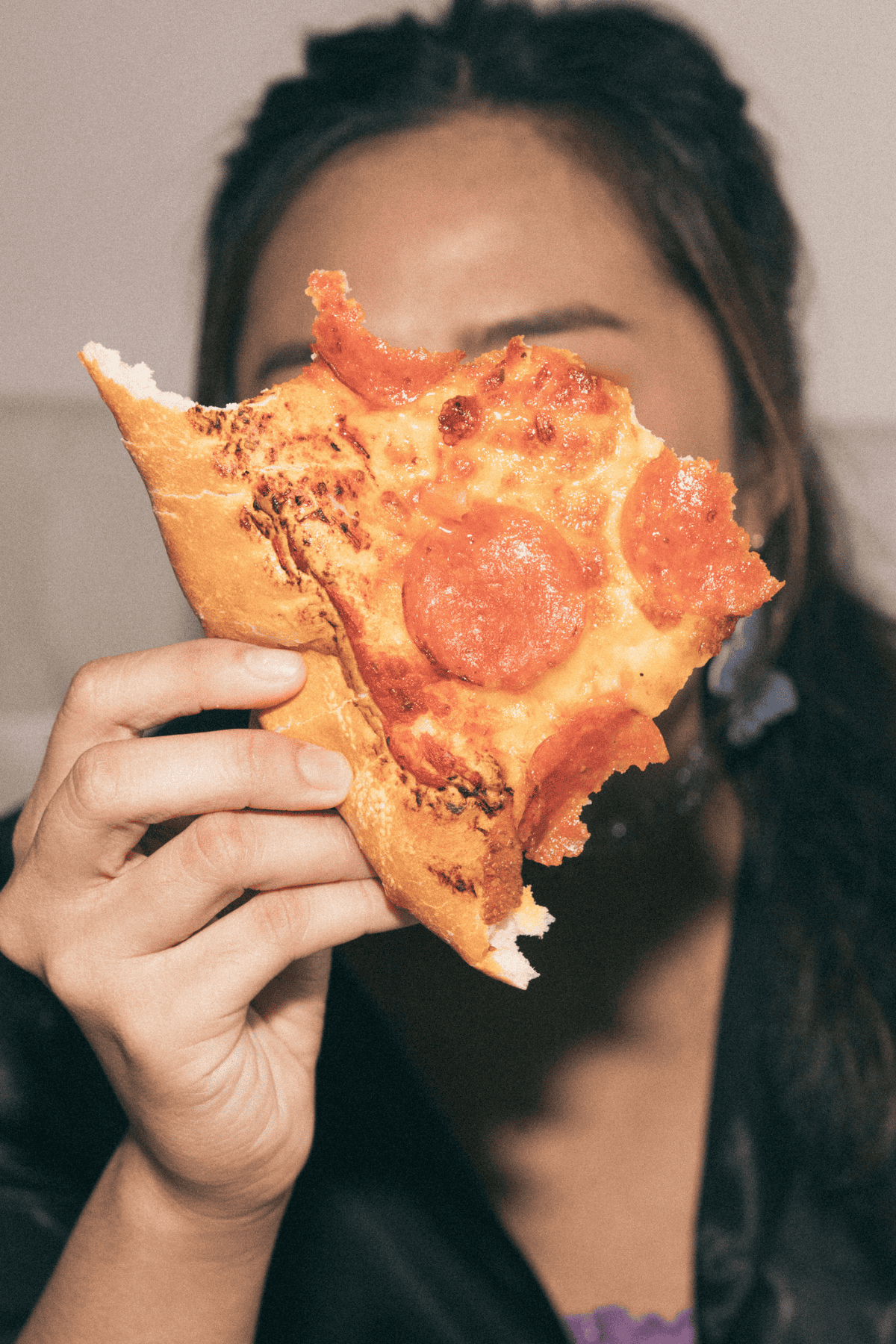 A female holding a piece of pizza in front of her face.