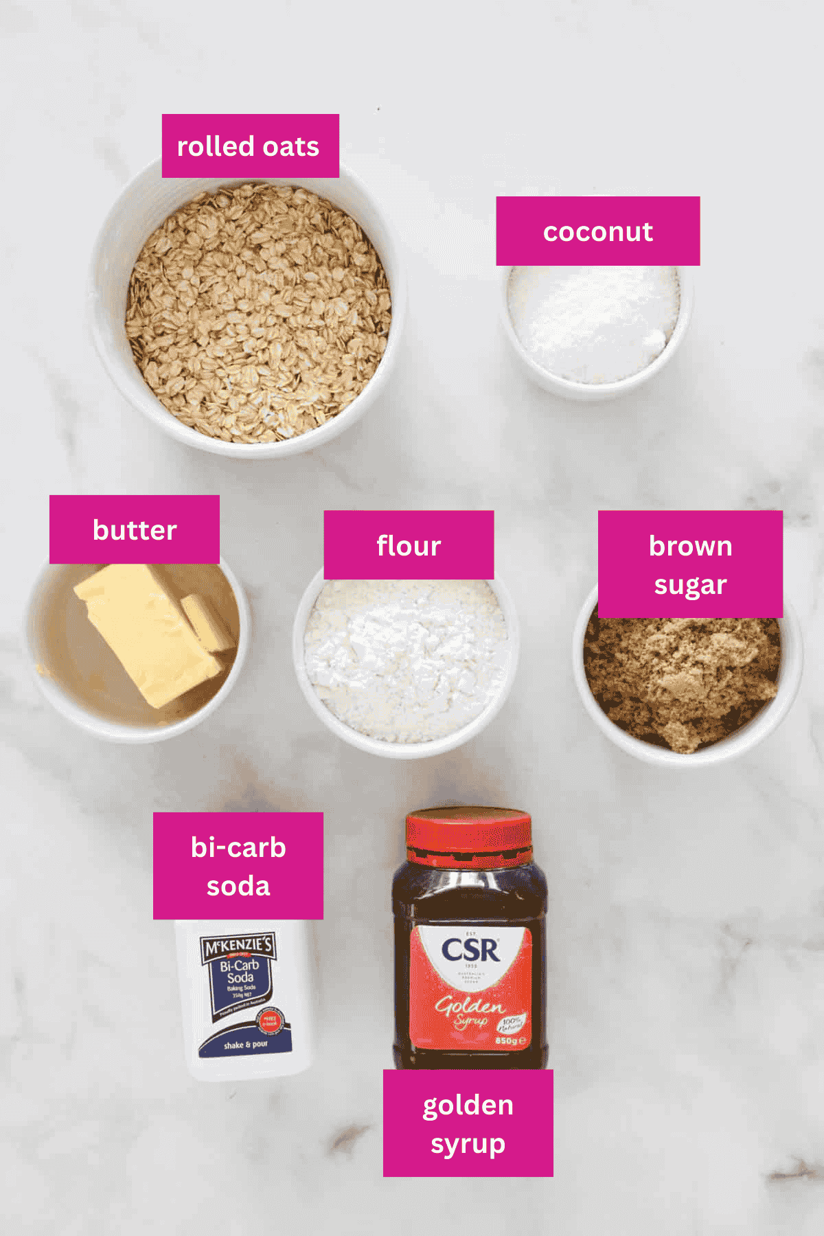 Rolled oats, flour, coconut, golden syrup, bicarb soda, brown sugar and butter in bowls.