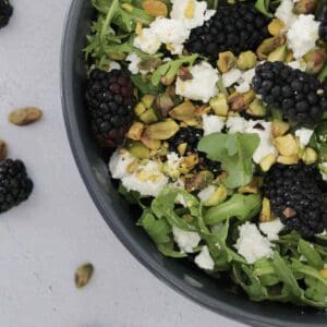 An overhead shot of a blackberry salad with pistachios, rocket and goat's cheese.