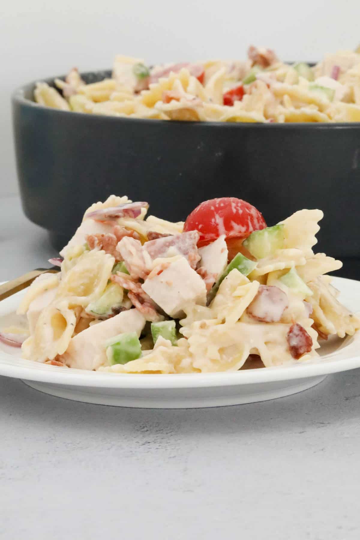 A bowl of ranch pasta salad with the serving bowl behind it.