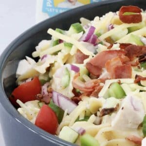A bowl of colourful salad with red onion, pasta, cherry tomatoes. chicken, bacon and cheese.