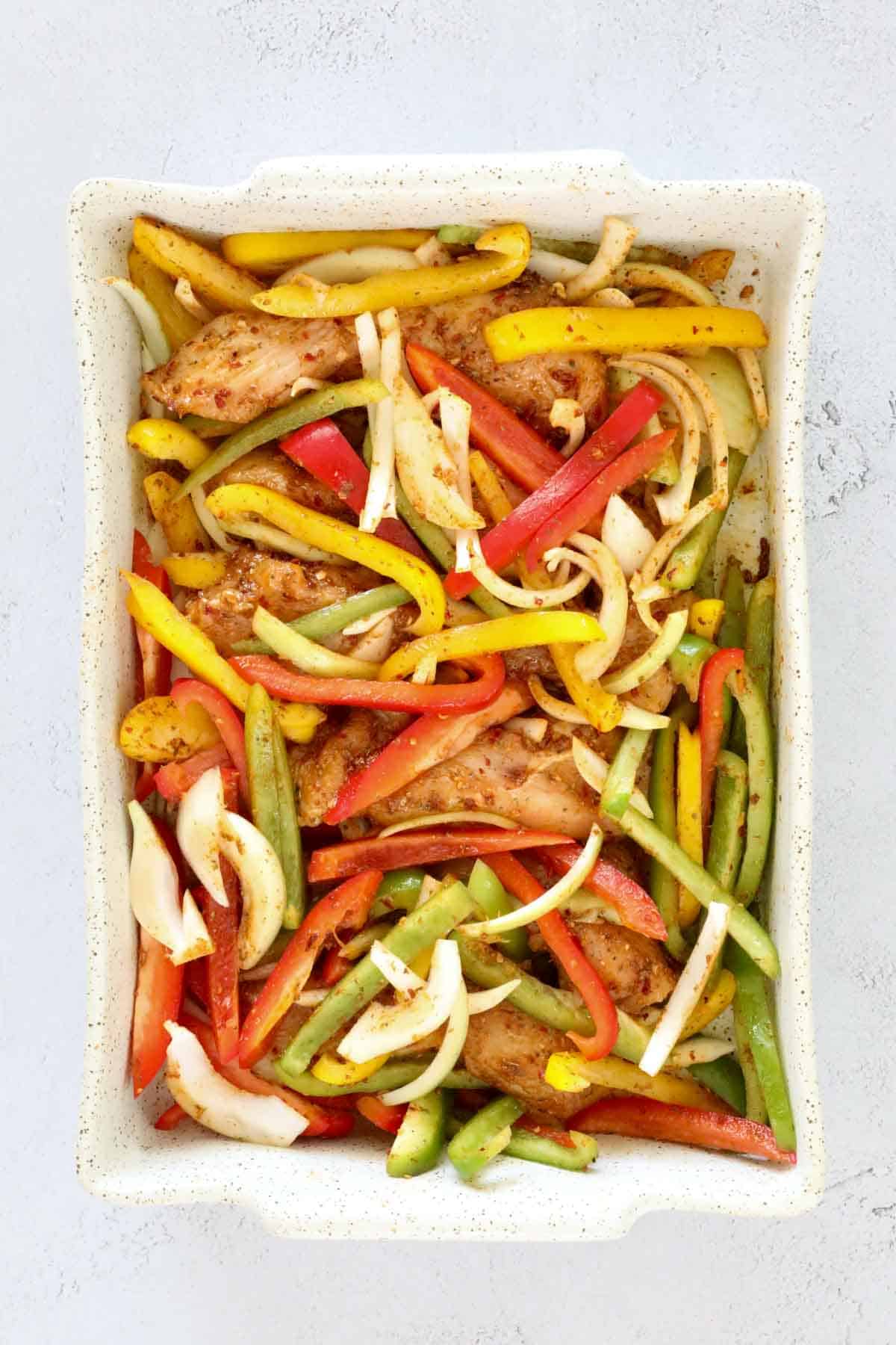 Fajita-seasoned chicken topped with sliced red, yellow, and green capsicum and onion in a baking dish.
