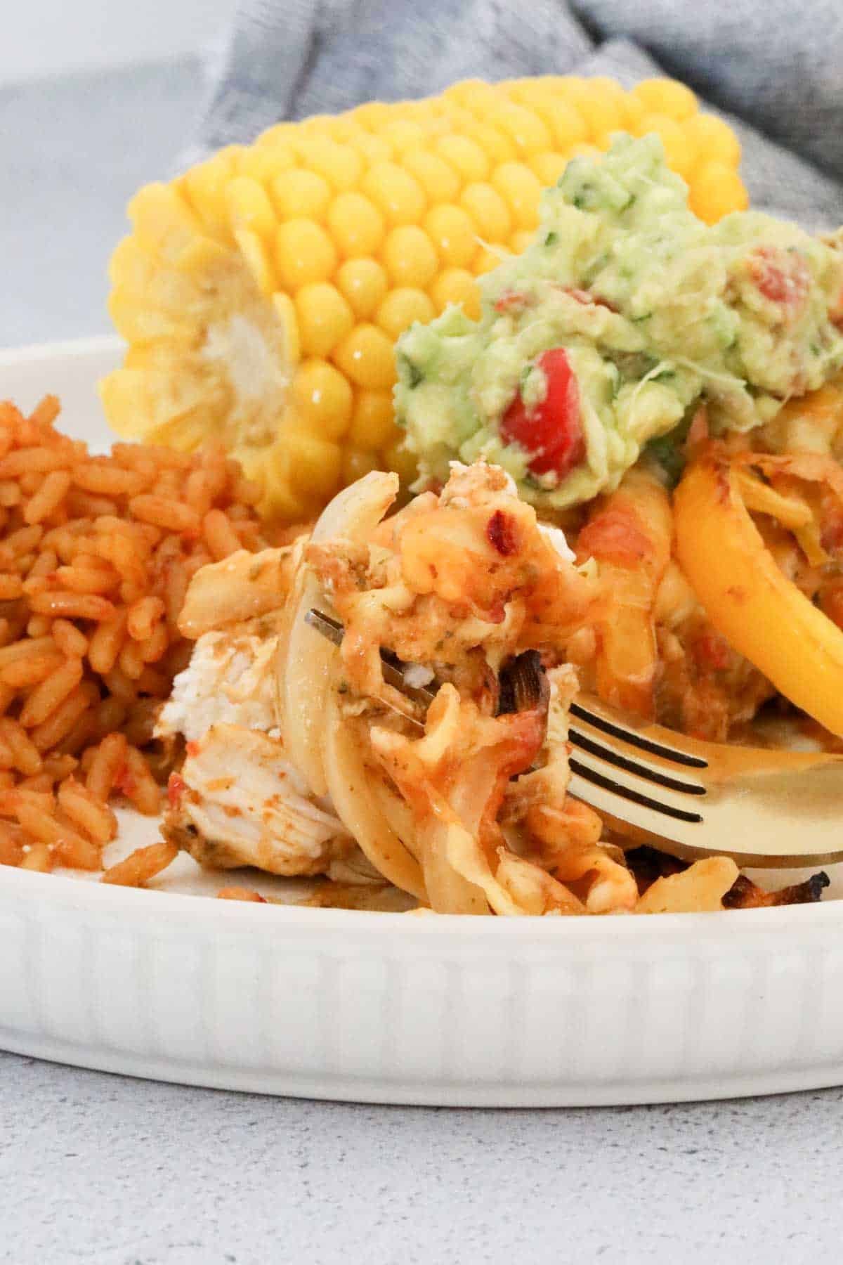 Forkful of chicken fajita casserole with onion and capsicum, served with rice and corn.