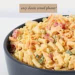 A dark grey serving bowl filled with colourful and creamy pasta salad.