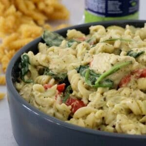 A bowl of creamy pesto pasta with chicken, tomatoes and spinach.