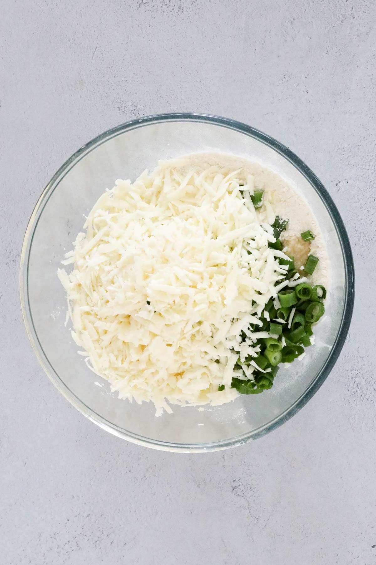 Cheese, spring onions on top of flour in a mixing bowl.