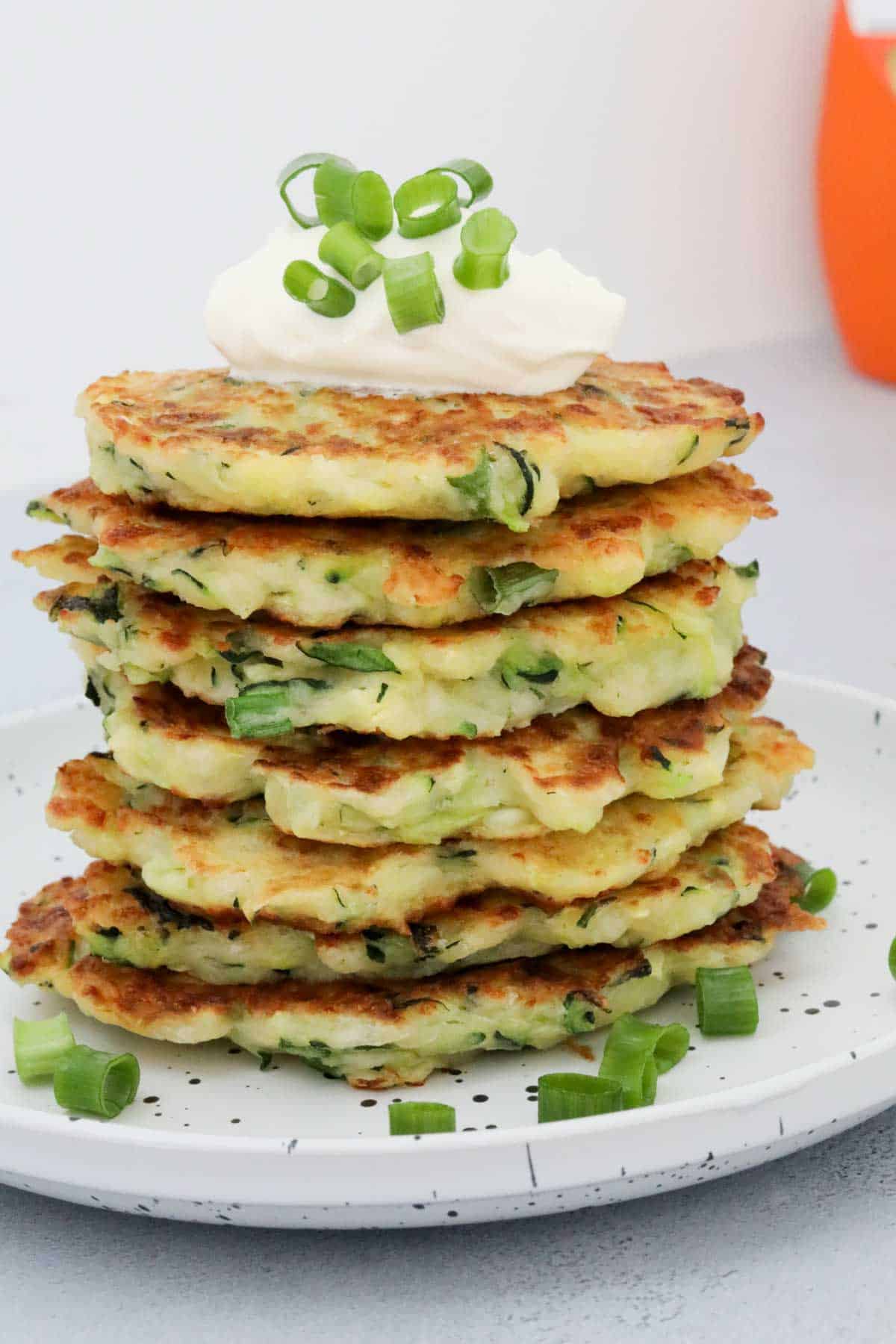 A stack of halloumi fritters on a plate, with a dollop of sour cream and sprinkled with chopped spring onions.