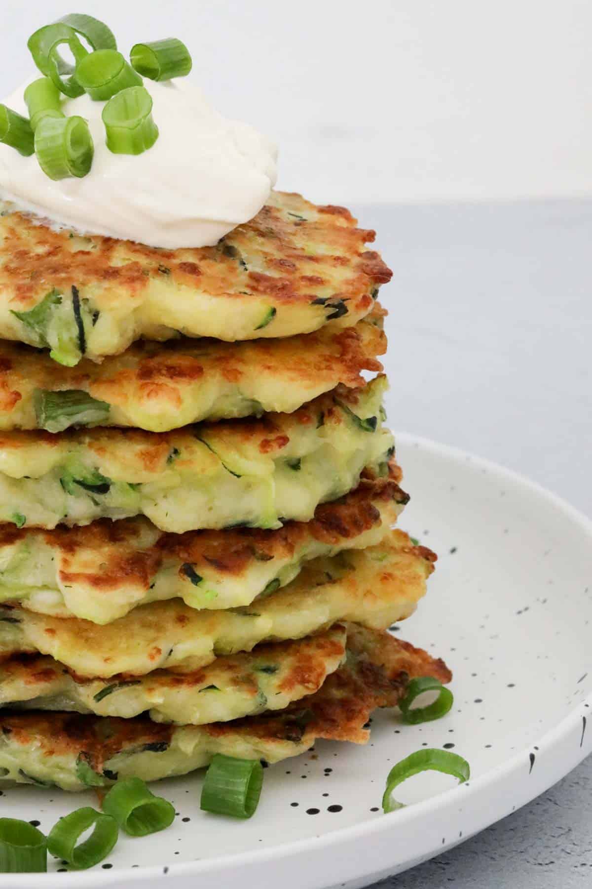 A stack of halloumi and zucchini fritters with sour cream on top.