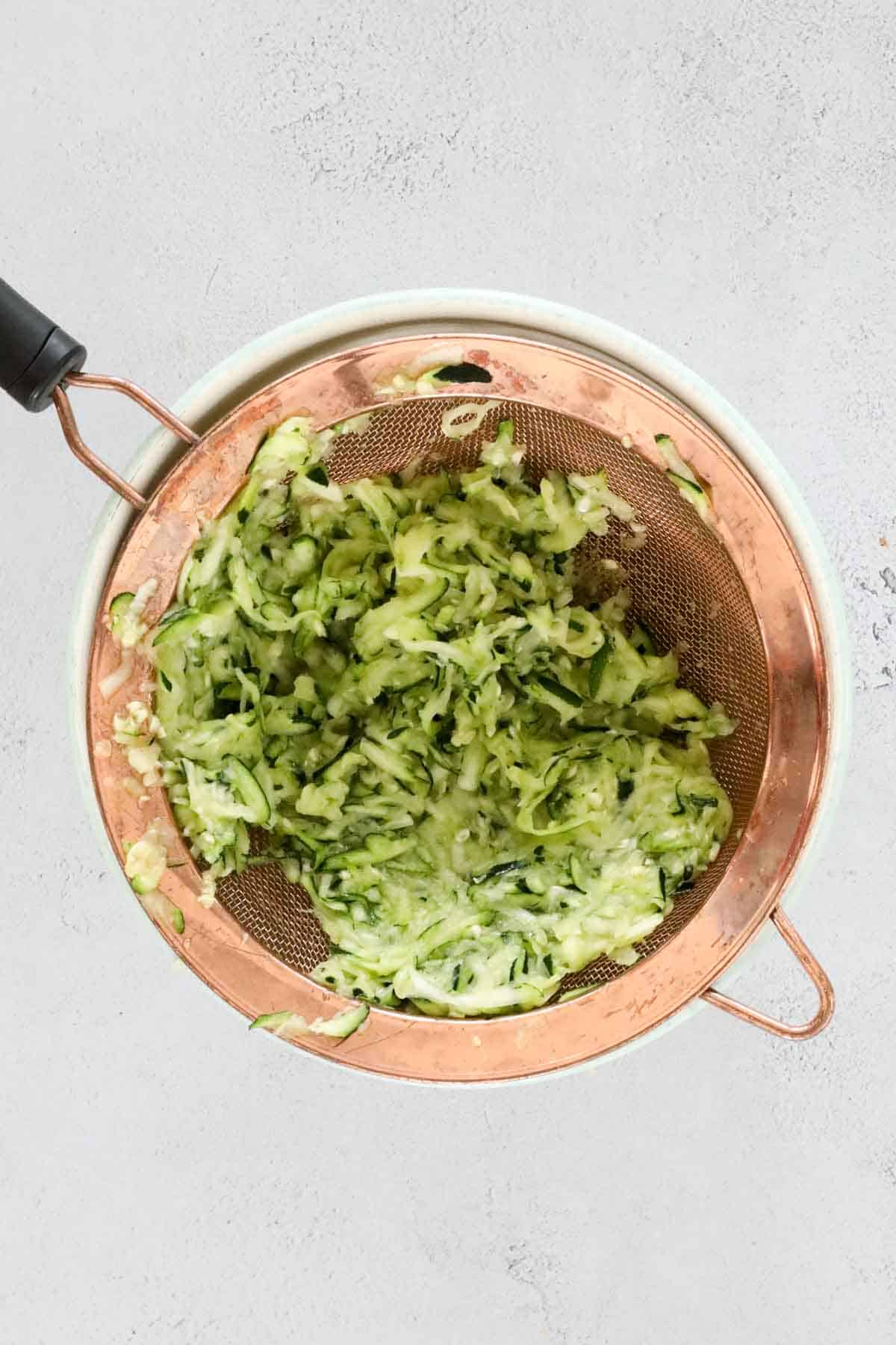 Grated zucchini a copper sieve.