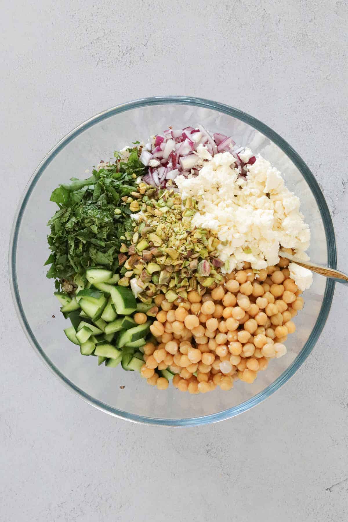 Feta, herbs, pistachios, red onion, chickpeas and cucumber in a bowl.