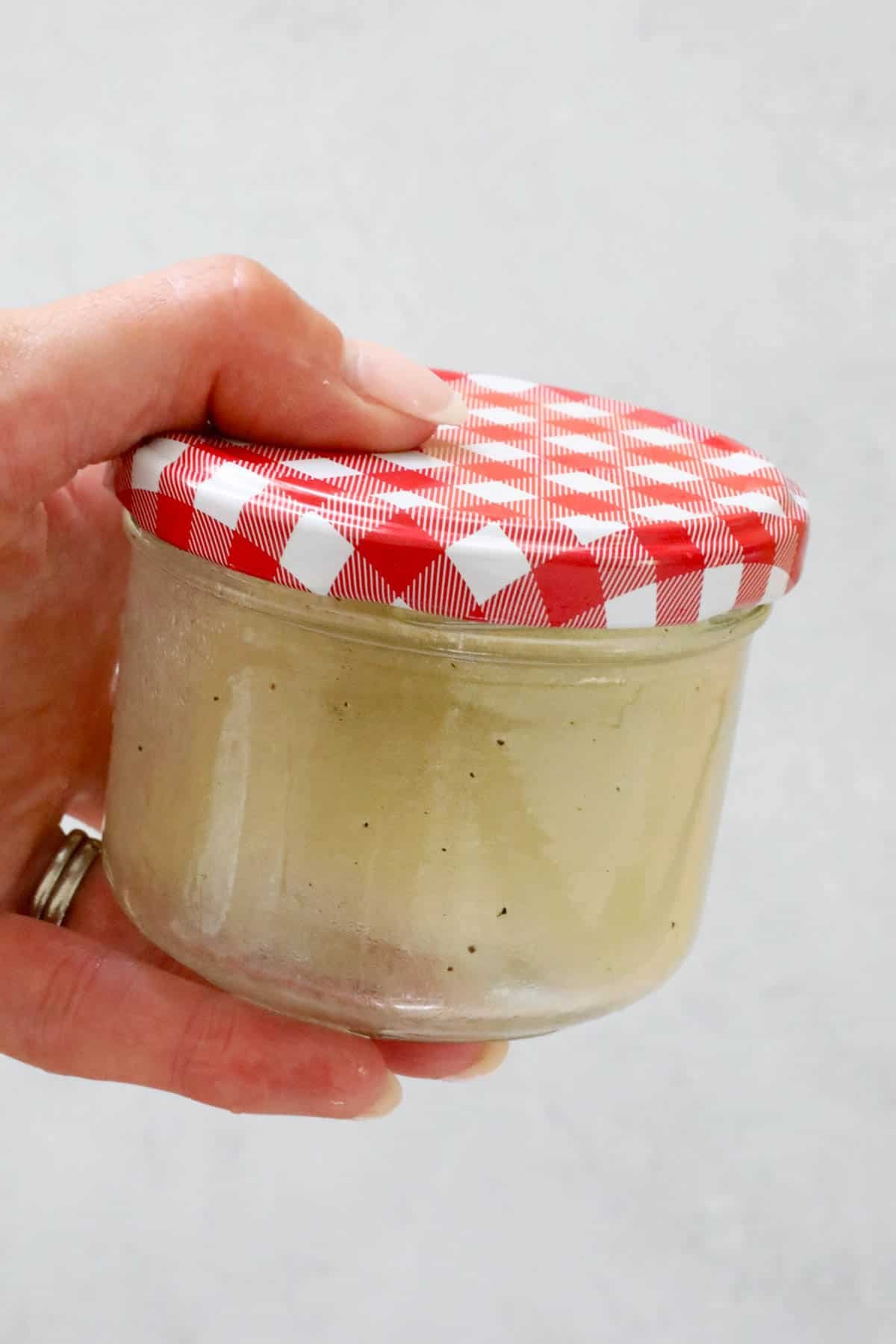 A hand holding a jar of dressing.