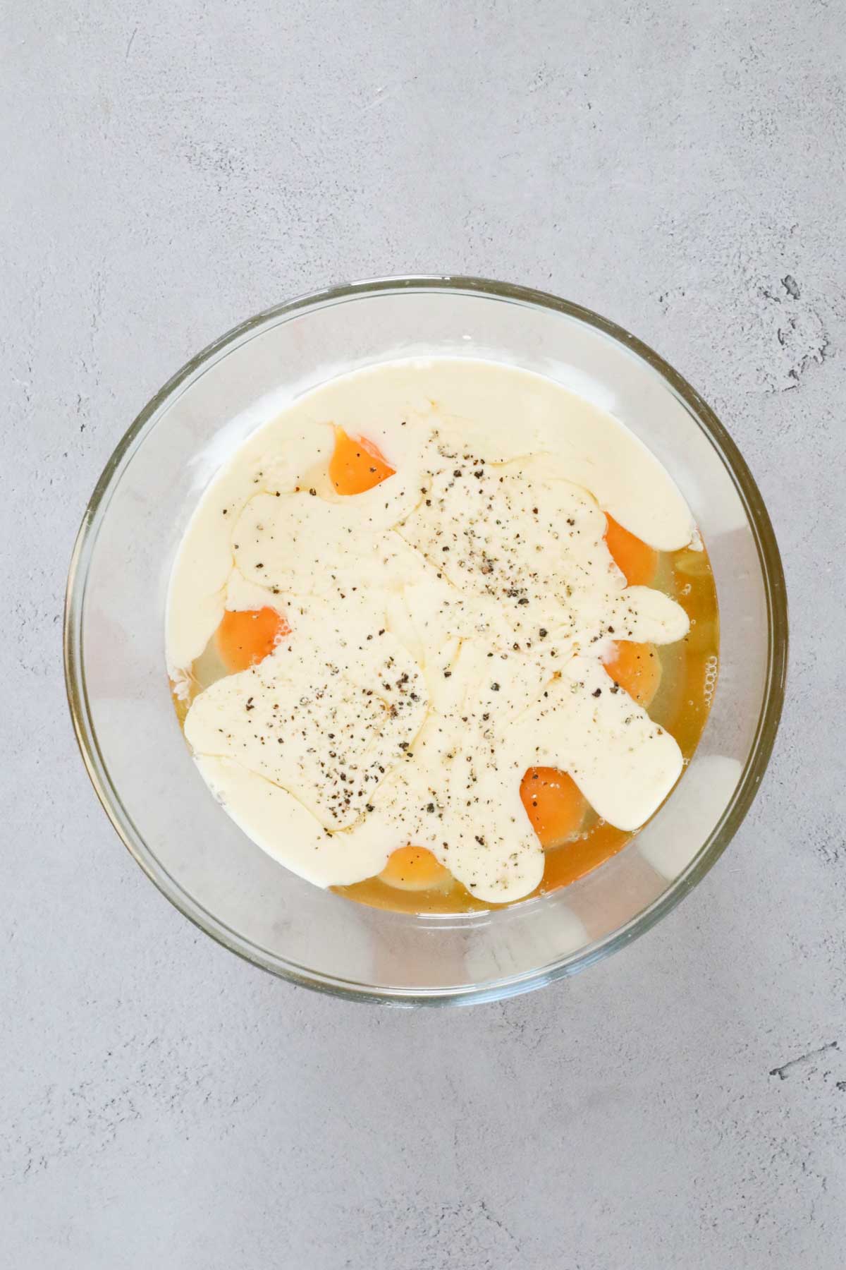 Eggs, cream and seasoning placed in a mixing bowl.