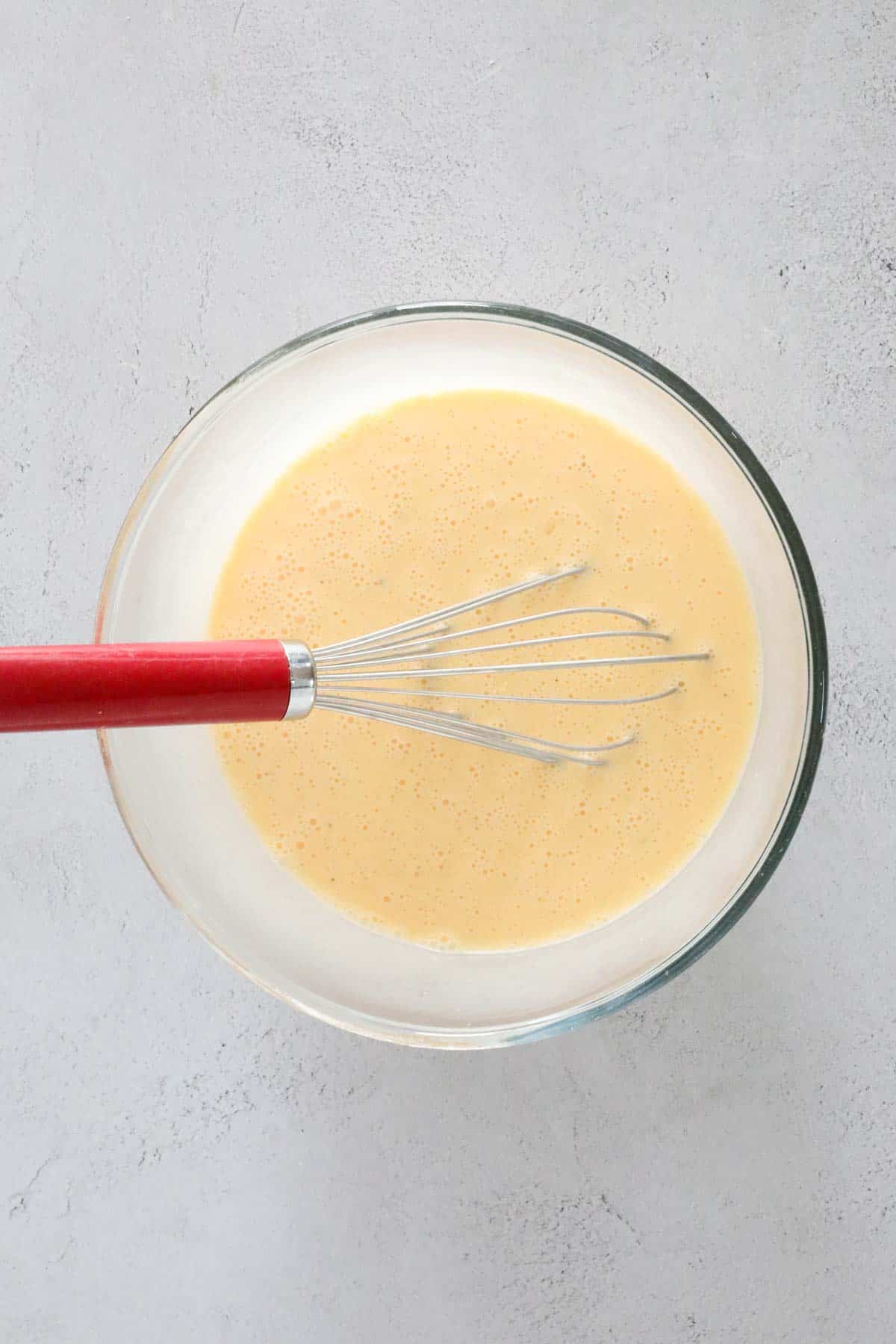 Eggs and cream whicked in a glass mixing bowl.