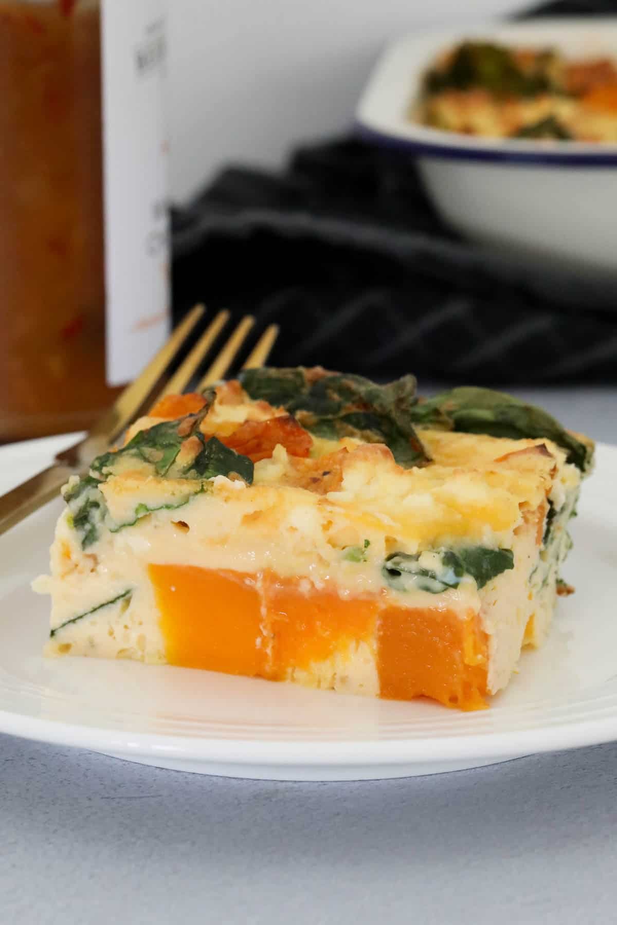 A square of pumpkin frittata on a white plate filled with spinach and feta. 