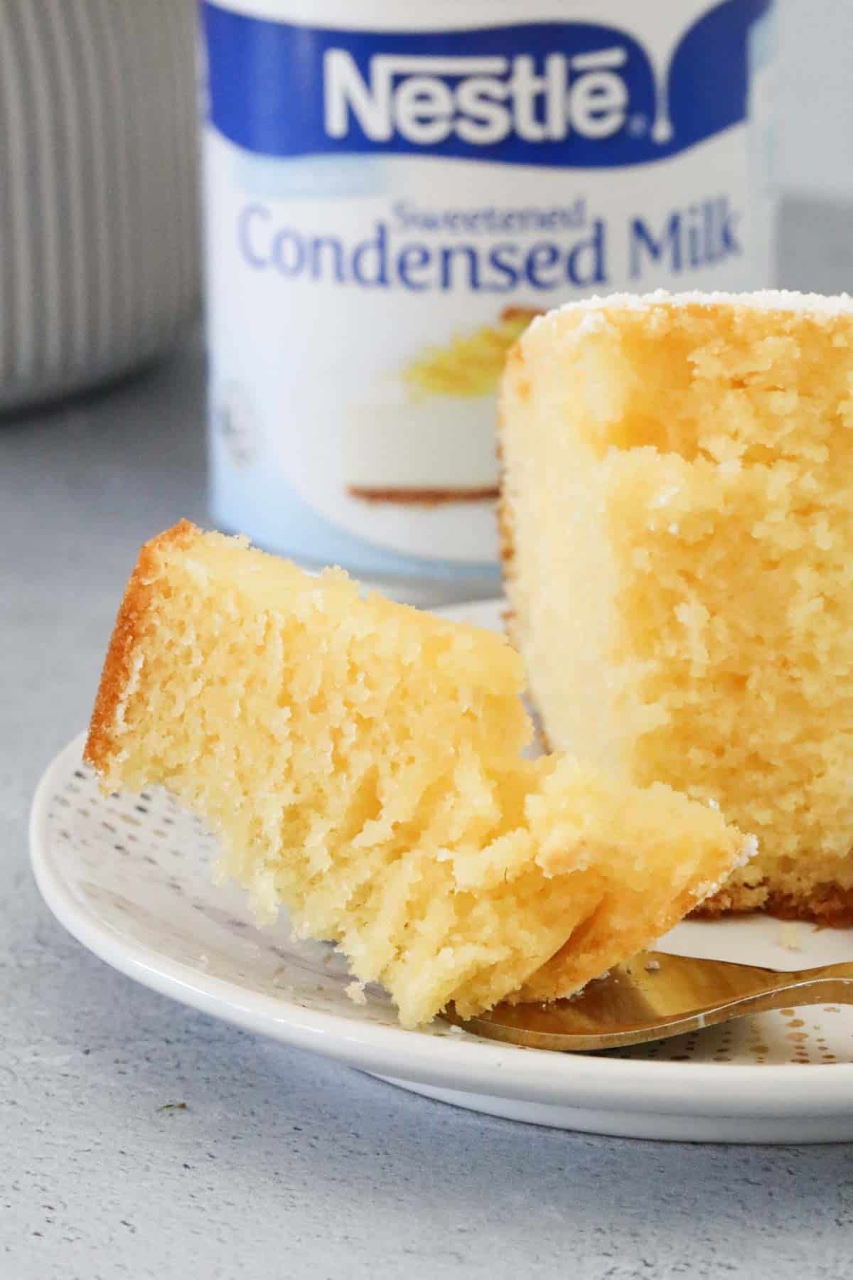 A piece of half eaten cake in front of a can of sweetened condensed milk.