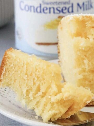 A piece of half eaten cake in front of a can of sweetened condensed milk.