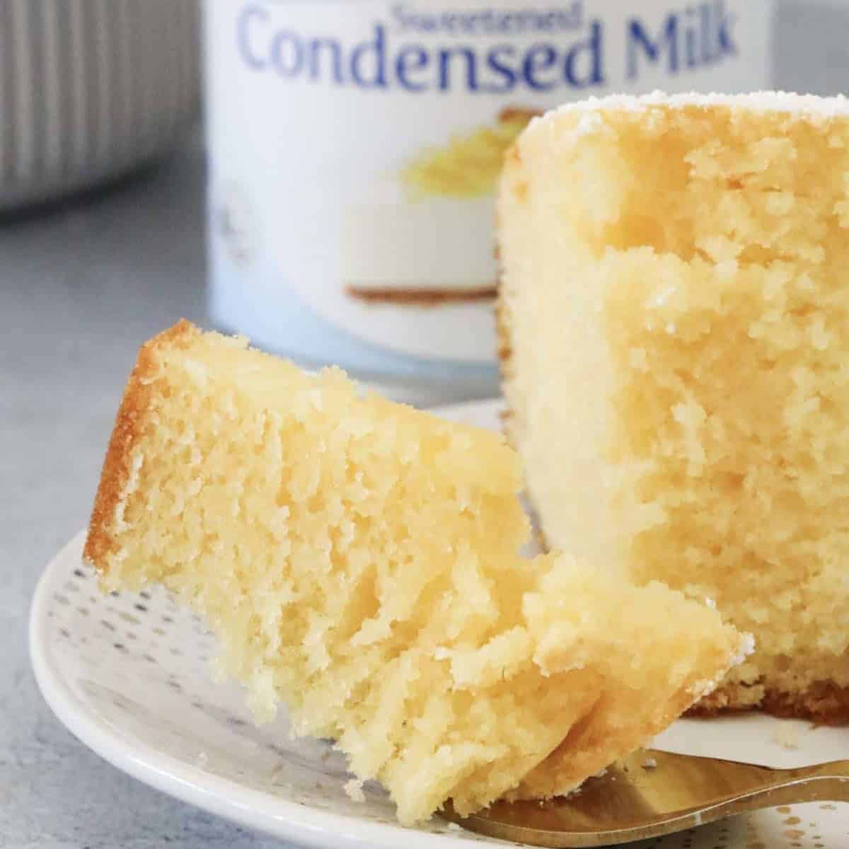 A piece of half eaten cake in front of a can of sweetened condensed milk.