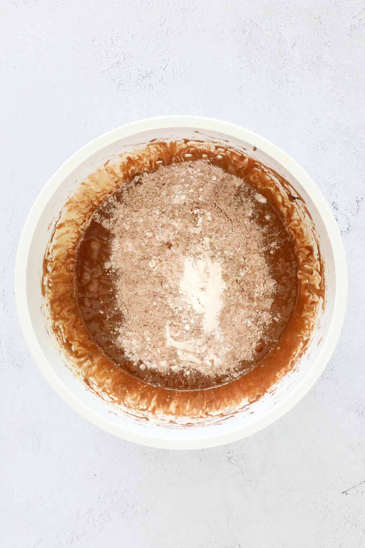 Flour and cocoa sifted over the wet mixture in a bowl.
