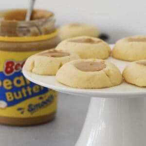 A cake stand of cookies filled with peanut butter in front of a jar of creamy peanut butter.