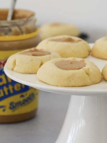 A cake stand of cookies filled with peanut butter in front of a jar of creamy peanut butter.
