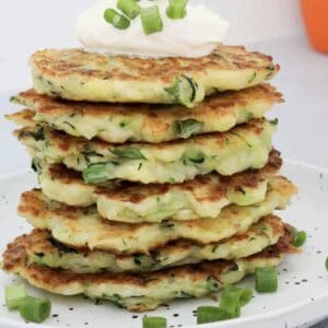 A stack of Halloumi & Zucchini Fritters with sour cream and spring onions on top.