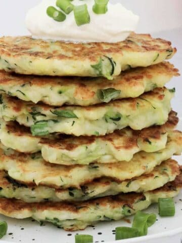 A stack of Halloumi & Zucchini Fritters with sour cream and spring onions on top.