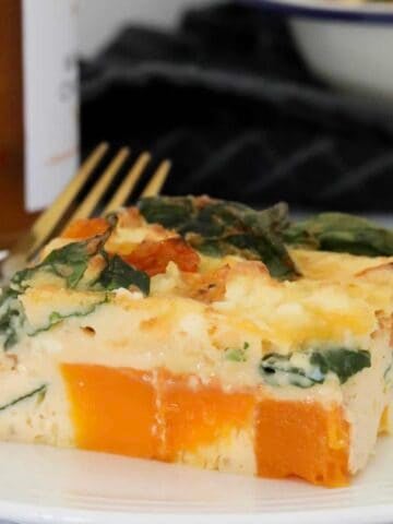 A piece of frittata with pumpkin, spinach and feta on a white plate.