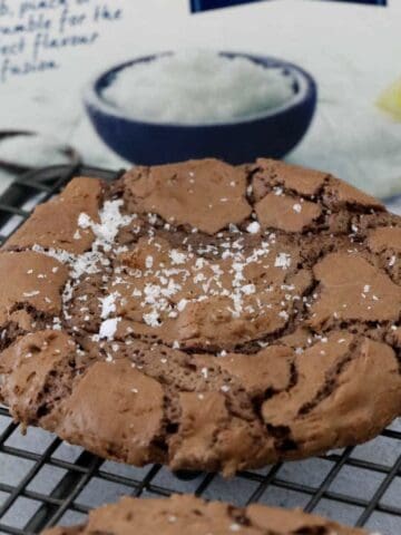 A chocolate crinkly cookie on a wire rack sprinkled with sea salt.