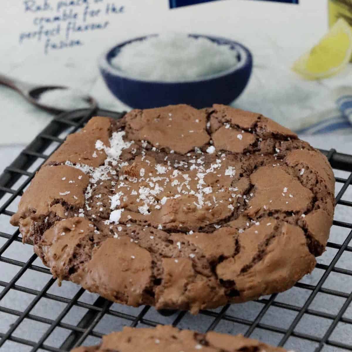 A chocolate crinkly cookie on a wire rack sprinkled with sea salt.